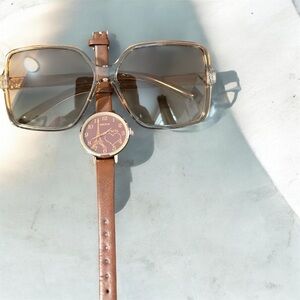 A brown leather strap watch with a heart-shaped dial and sunglasses.